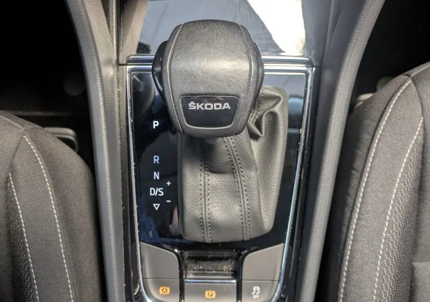 Vue rapprochée du levier de vitesse automatique noir marqué ŠKODA, entouré de sièges en tissu gris foncé.