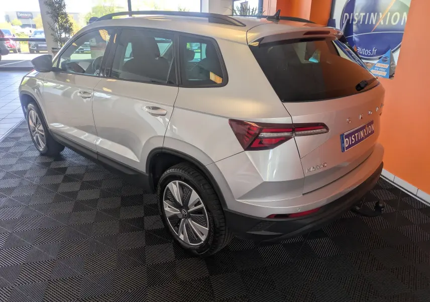 Vue 3/4 arrière droite d'un Skoda Karoq gris argent 2023 avec jantes alliage et hayon électrique en intérieur showroom.