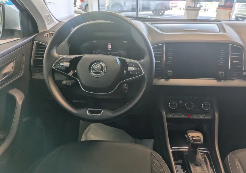 Vue intérieure centrée sur le volant noir et le tableau de bord avec écran tactile du Skoda Karoq gris argent 2023.