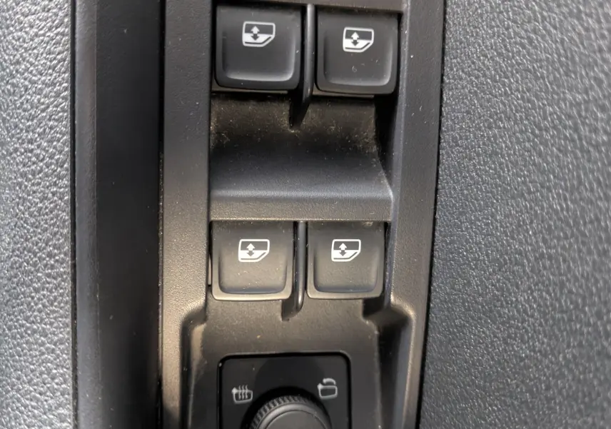 Gros plan sur les commandes des vitres électriques et réglage des rétroviseurs dans l'habitacle noir du Skoda Karoq 2023.