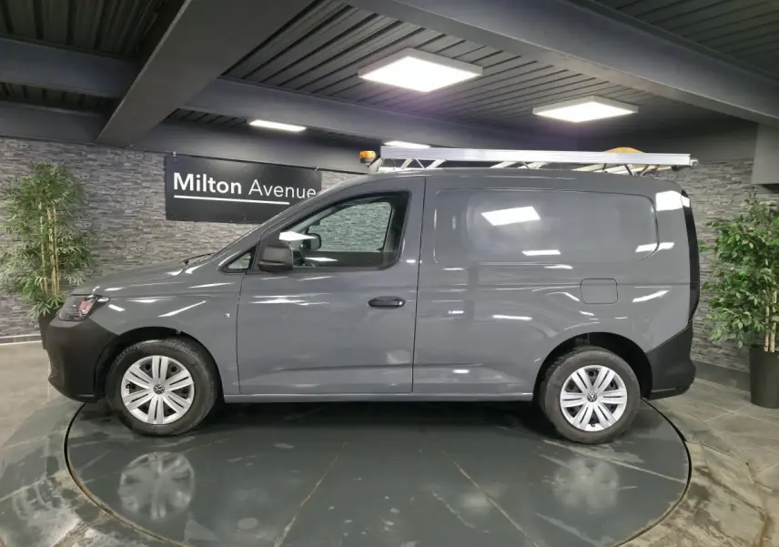 Vue latérale droite d’un Volkswagen Caddy Cargo gris 2022 avec galerie de toit et jantes acier noires.