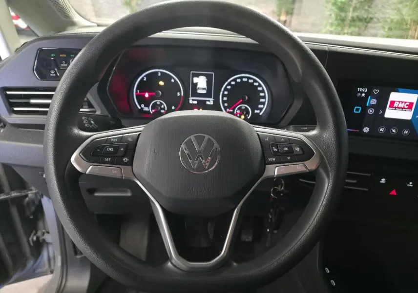 Vue intérieure centrée sur le volant noir du Volkswagen Caddy Cargo 2022 avec tableau de bord et écran tactile.