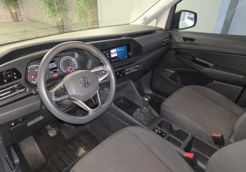Vue intérieure côté conducteur du Volkswagen Caddy Cargo 2022, tableau de bord noir et sièges tissu gris foncé.