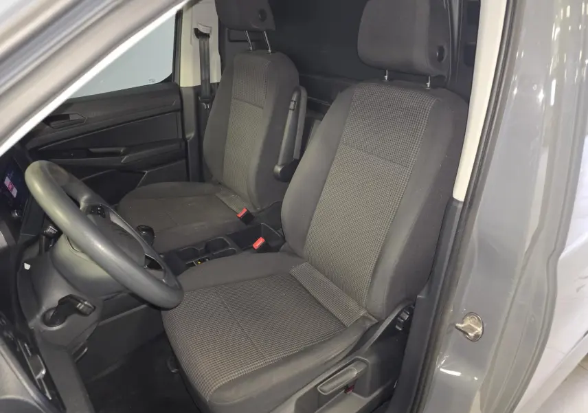 Vue intérieure côté conducteur du Volkswagen Caddy Cargo gris 2022, montrant les sièges avant en tissu et la cloison de séparation.