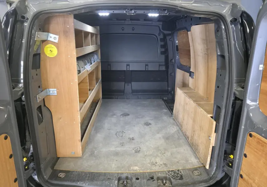 Vue intérieure arrière du Volkswagen Caddy Cargo gris 2022, montrant l'espace de chargement avec étagères en bois.