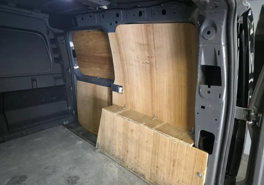 Vue intérieure côté droit du fourgon Volkswagen Caddy Cargo gris 2022 avec cloison bois et plancher caoutchouc.