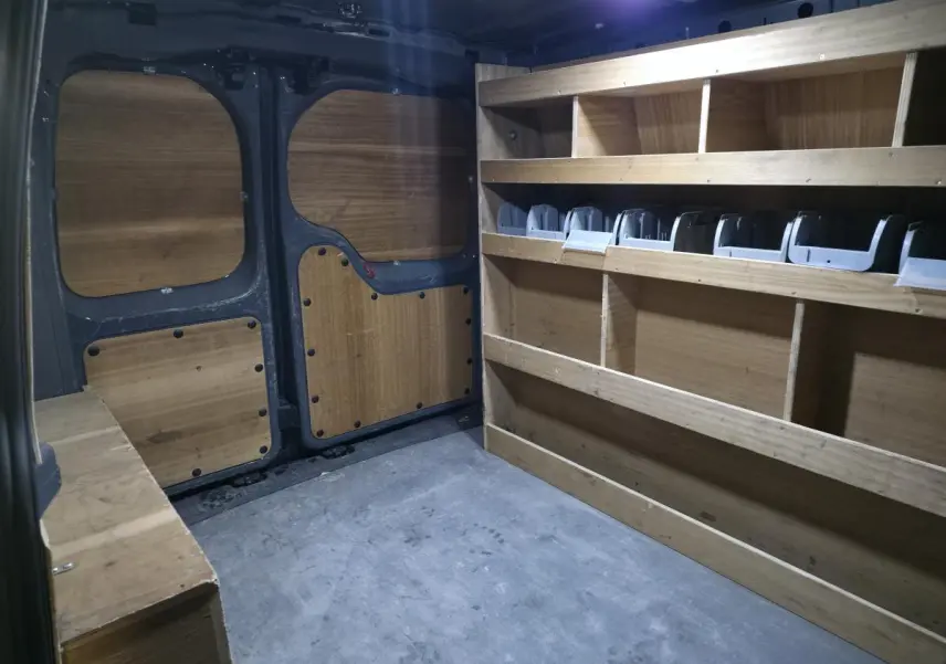 Vue intérieure arrière du fourgon Volkswagen Caddy Cargo gris, montrant les aménagements en bois pour rangement.