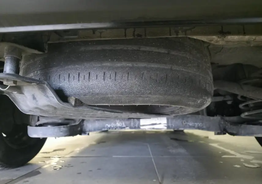 Vue en contre-plongée sous un Volkswagen Caddy Cargo gris montrant la roue de secours et le train arrière.