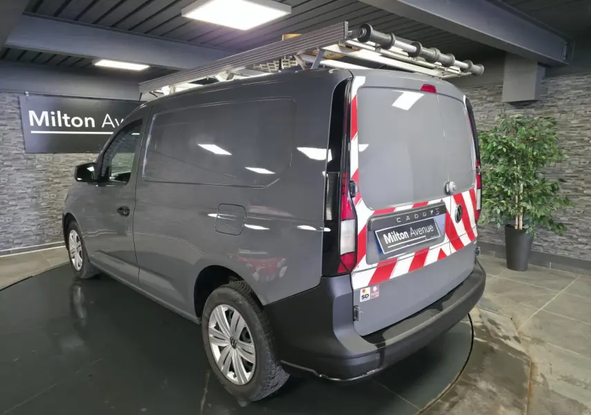 Vue 3/4 arrière droite d’un Volkswagen Caddy Cargo gris avec marquage rouge et blanc sur les portes arrière et galerie de toit.