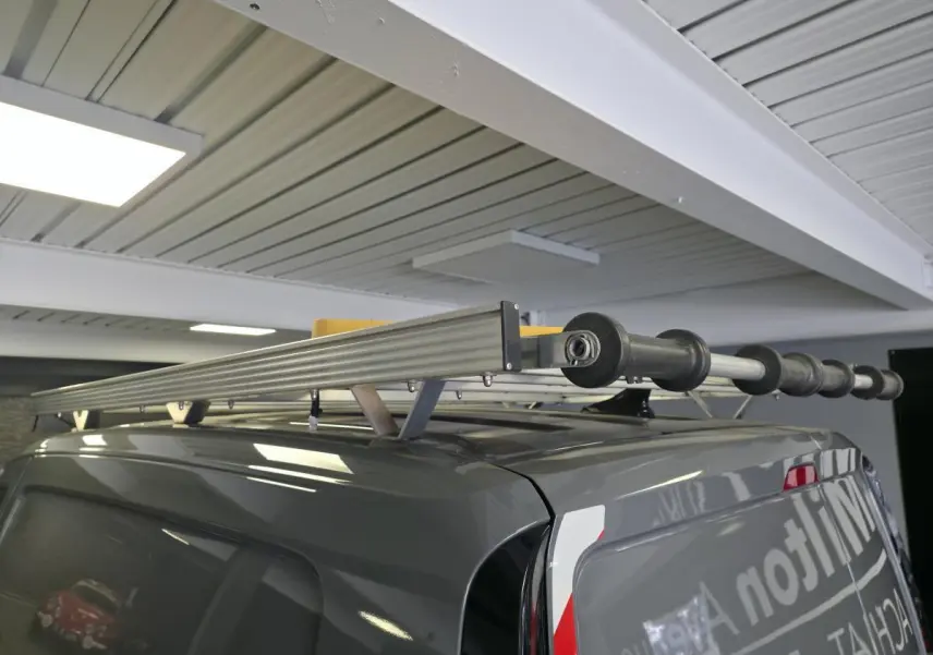 Vue arrière en 3/4 droit d’un Volkswagen Caddy Cargo gris avec galerie de toit et échelle fixée dessus dans un garage.