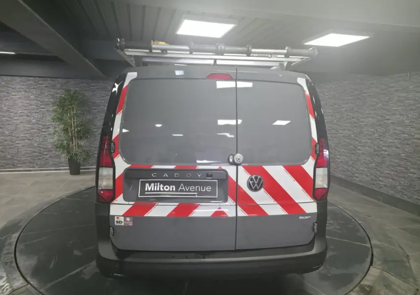 Vue arrière d’un Volkswagen Caddy Cargo gris 2022 avec bandes réfléchissantes rouges et blanches et galerie de toit.