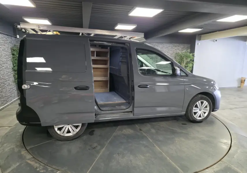 Vue latérale droite d'un Volkswagen Caddy Cargo gris 2022 avec porte coulissante ouverte révélant un aménagement bois intérieur.