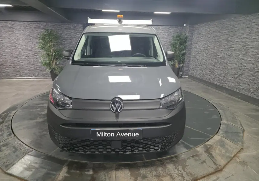 Vue frontale d'un Volkswagen Caddy Cargo gris 2022 avec galerie de toit et feux halogènes allumés en intérieur.
