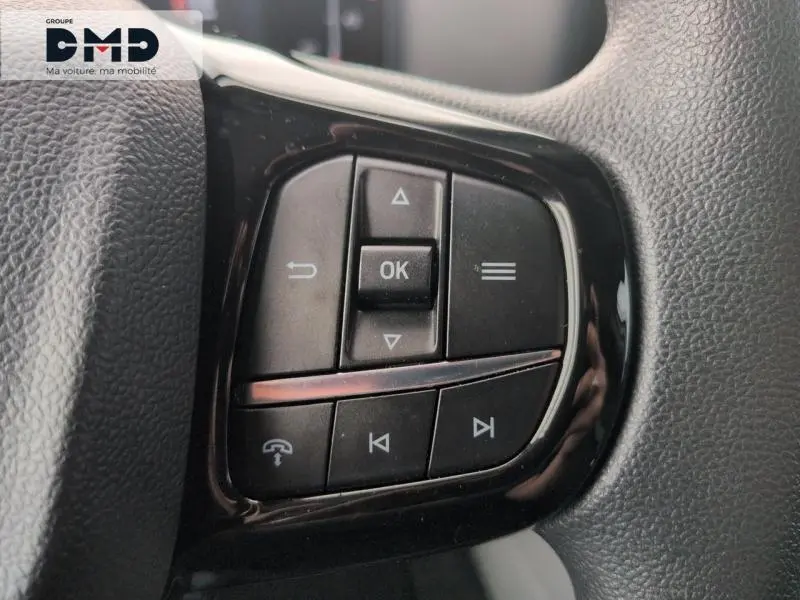 Gros plan sur les commandes audio au volant noir du Ford Transit Custom Fourgon blanc Glacier 2024.