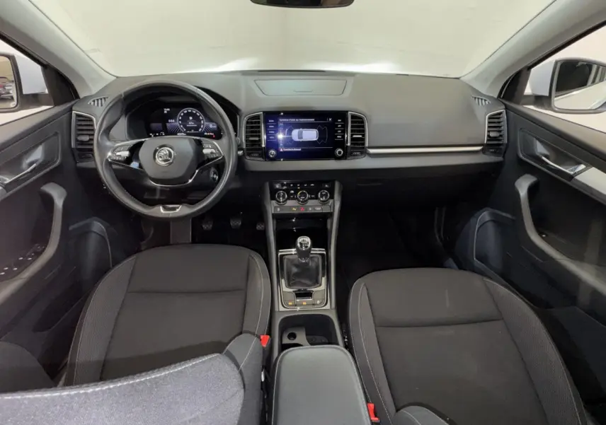 Vue intérieure avant du Skoda Karoq 2024, tableau de bord noir avec écran tactile central et volant cuir multifonctions.