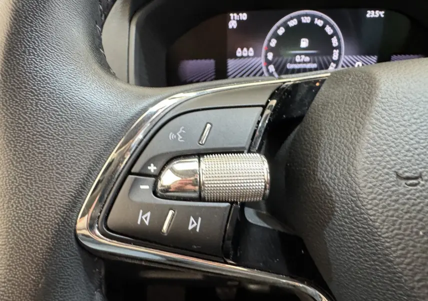 Gros plan sur la commande multifonction gauche du volant cuir du Skoda Karoq 2024 avec affichage numérique en arrière-plan.