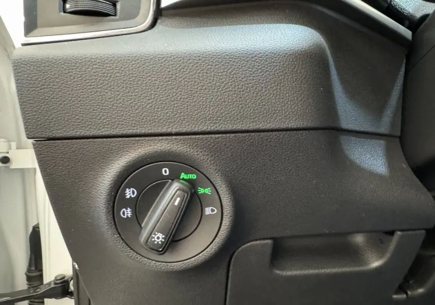 Gros plan sur le bouton de commande des phares avec réglage automatique dans l'habitacle noir d'une Skoda Karoq blanc.