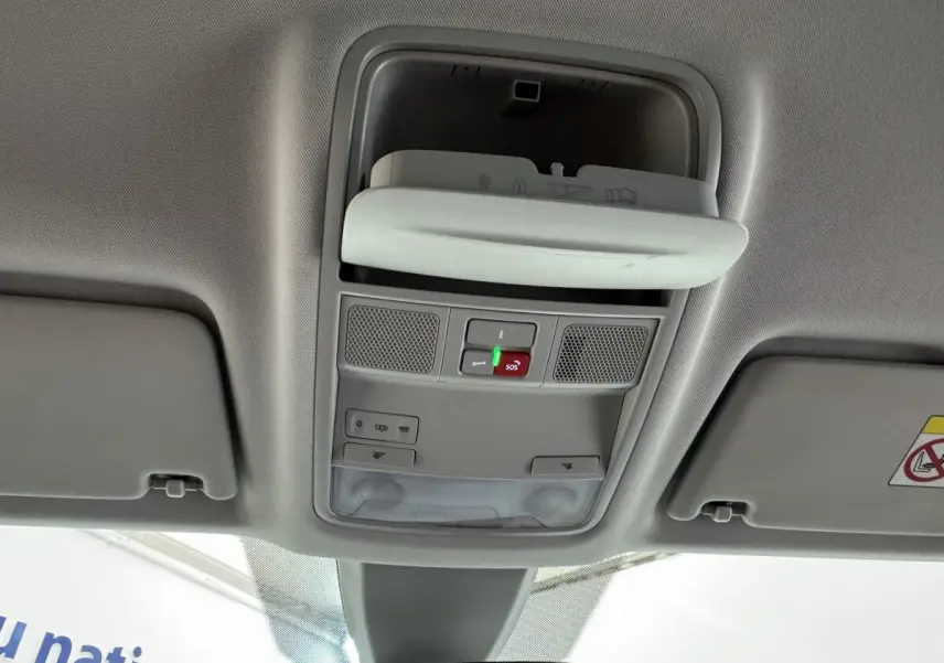 Vue intérieure du plafond avant du Skoda Karoq blanc 2024, montrant les commandes d'éclairage et le rangement lunettes ouvert.