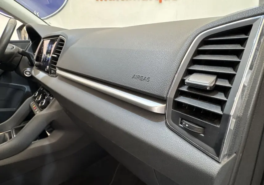 Vue intérieure côté passager du tableau de bord noir du Skoda Karoq 2024 avec aérateurs et écran tactile visible.