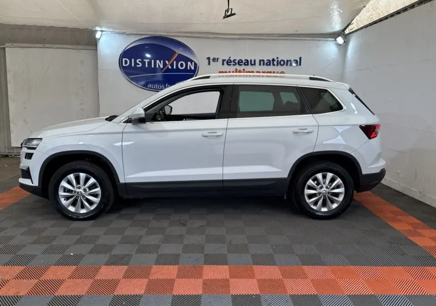 Vue latérale droite d'un Skoda Karoq blanc 2024, SUV compact avec jantes alliage et barres de toit noires.