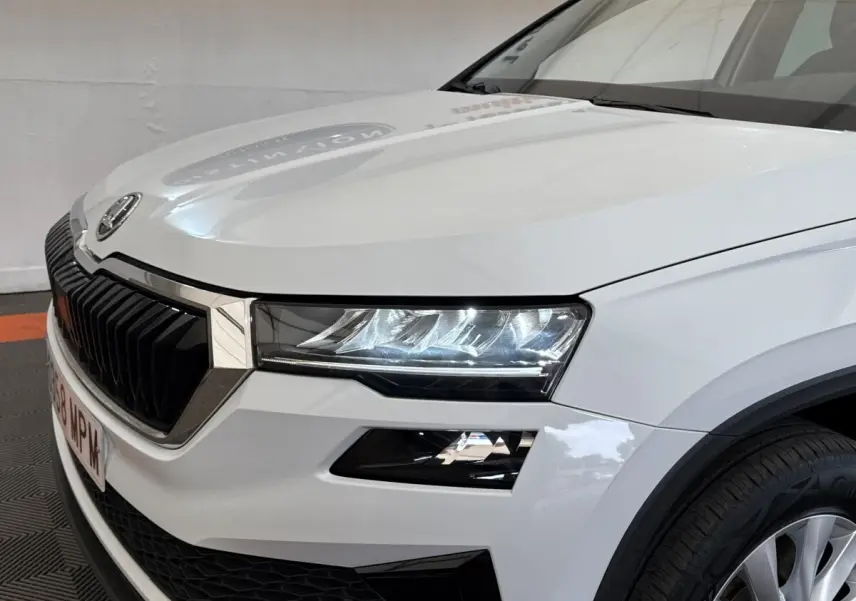 Vue 3/4 avant droit d'un Skoda Karoq blanc 2024 avec calandre noire et phares LED distinctifs.