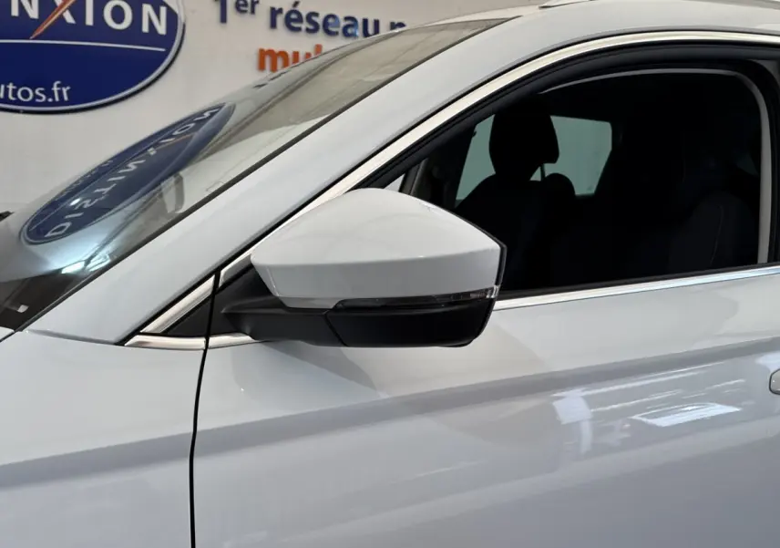 Gros plan sur le rétroviseur côté gauche d’un Skoda Karoq blanc 2024 avec fenêtre ouverte et contours noirs.