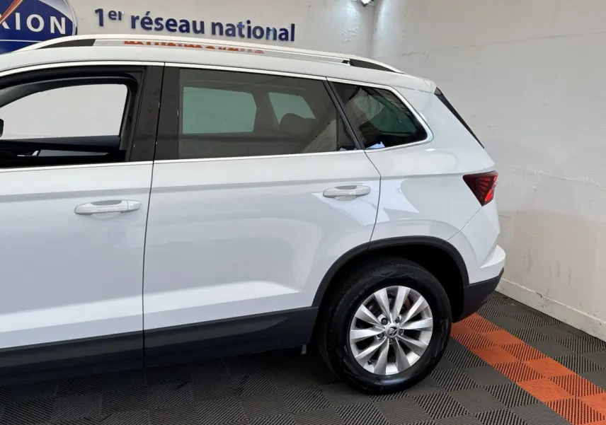 Vue latérale côté droit du SUV blanc SKODA KAROQ 2024 avec jantes alliage et rails de toit noirs visibles.
