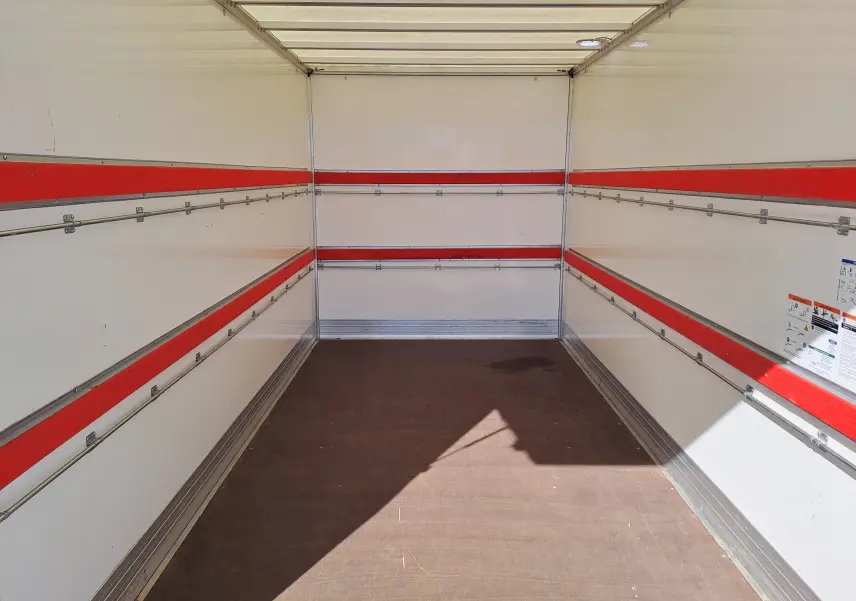 Intérieur du coffre blanc du Nissan Interstar Châssis Cabine L3H1 2024, vue de l'arrière avec bandes rouges et sol en bois.