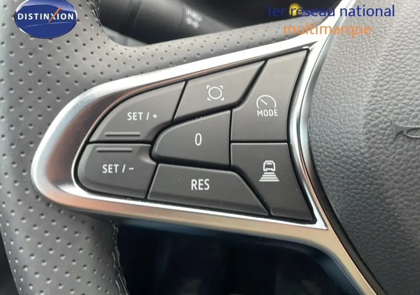 Gros plan sur les commandes du volant perforé du Renault Captur blanc nacré, version hybride 2025, avec boutons multifonctions.