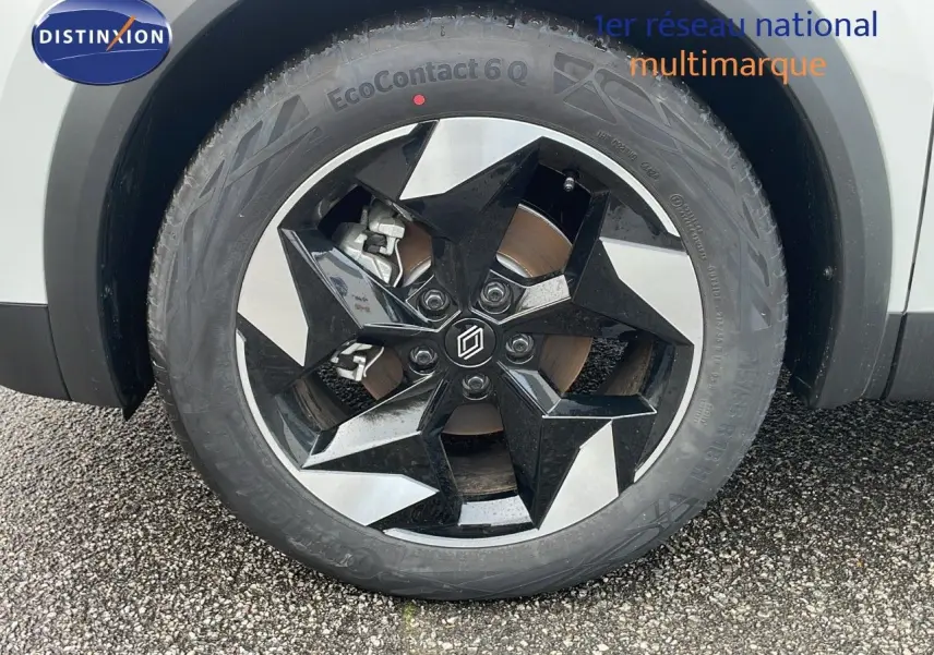 Gros plan sur la roue avant gauche du Renault Captur blanc nacré avec jante noire et argentée au design étoilé.