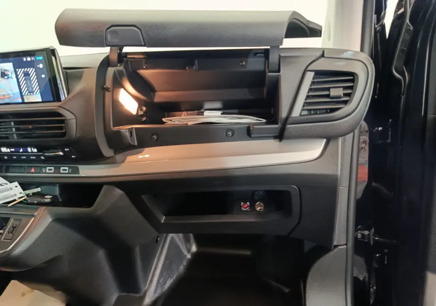 Vue intérieure du tableau de bord du Citroën Jumpy XL noir 2025, boîte à gants ouverte avec éclairage intérieur visible.