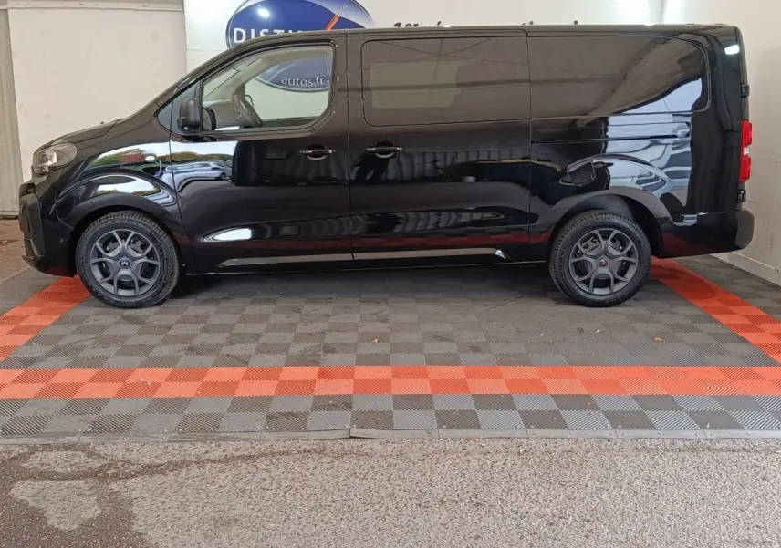 Profil côté gauche d'un Citroën Jumpy XL noir 2025 avec jantes spécifiques et vitres teintées en intérieur showroom.