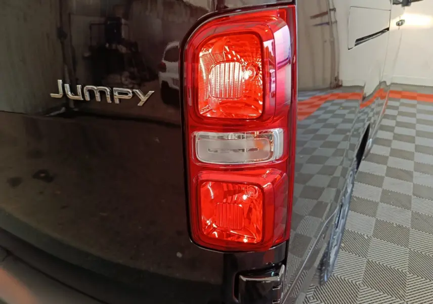 Gros plan sur le feu arrière droit et le logo Jumpy d’un Citroën Jumpy XL noir stationné en intérieur.