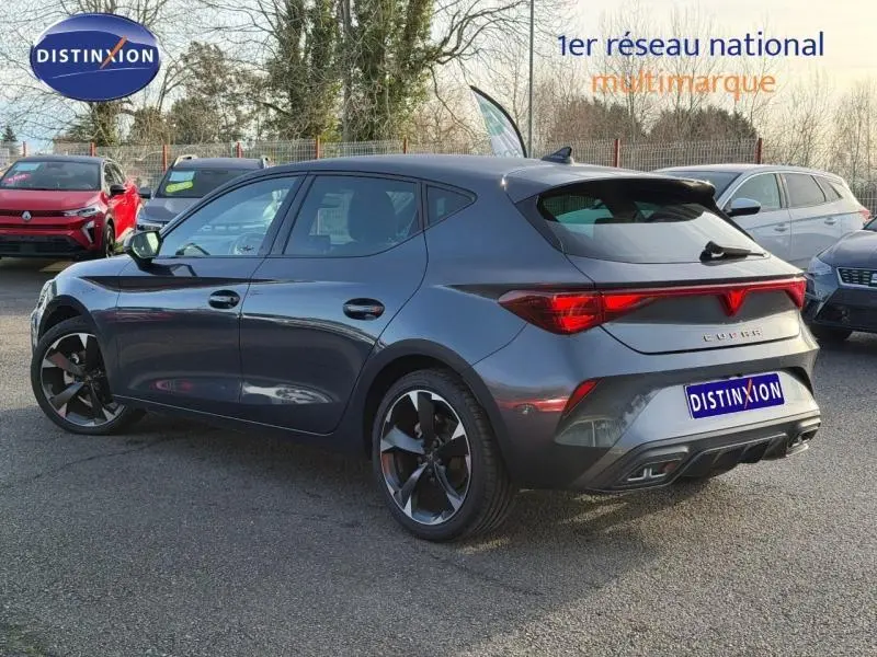 Vue 3/4 arrière droite d'une SEAT LEON 1.5 eTSI Hybrid 2025 gris magnétique métal avec feux arrière reliés et jantes noires.