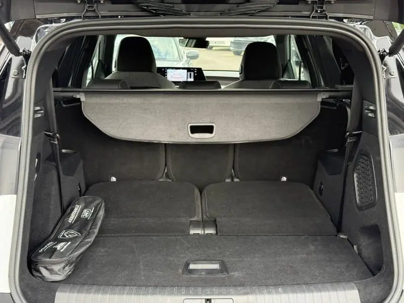 Vue intérieure du coffre ouvert du Peugeot 5008 Hybrid blanc, montrant les sièges arrière rabattus et une trousse d'assistance noire.