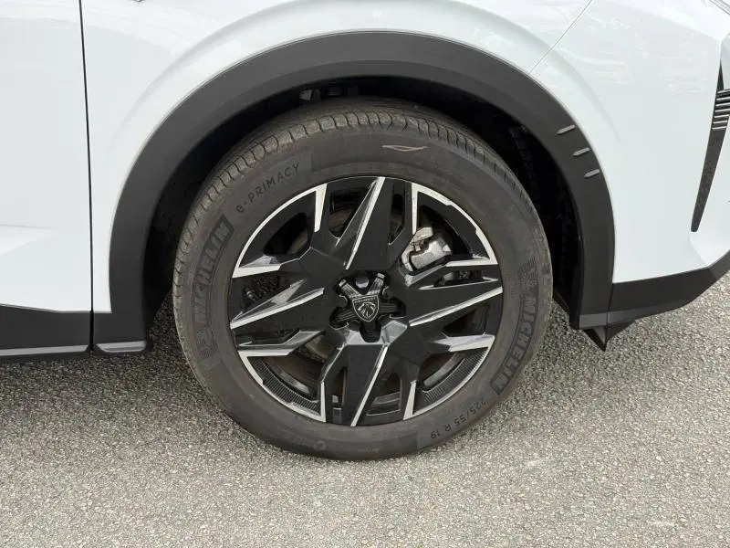 Gros plan sur la roue avant droite du Peugeot 5008 Hybrid blanc Okénite, avec jante noire et détails argentés.