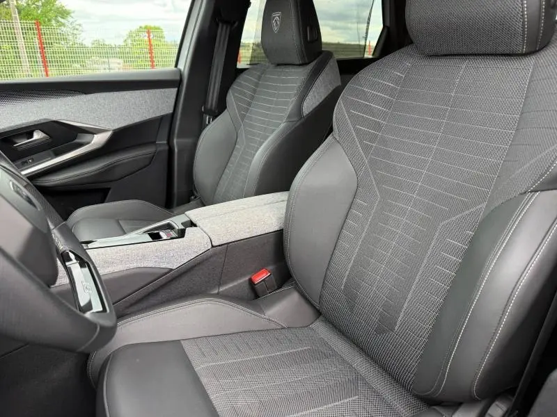 Vue intérieure rapprochée des sièges avant gris foncé avec logo Peugeot brodé sur appuie-tête du 5008 Hybrid 2025.