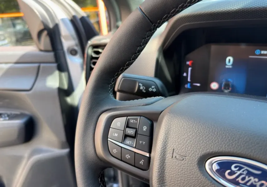 Gros plan sur le volant cuir multifonctions du Ford Ranger gris iconic, avec tableau de bord numérique en arrière-plan.