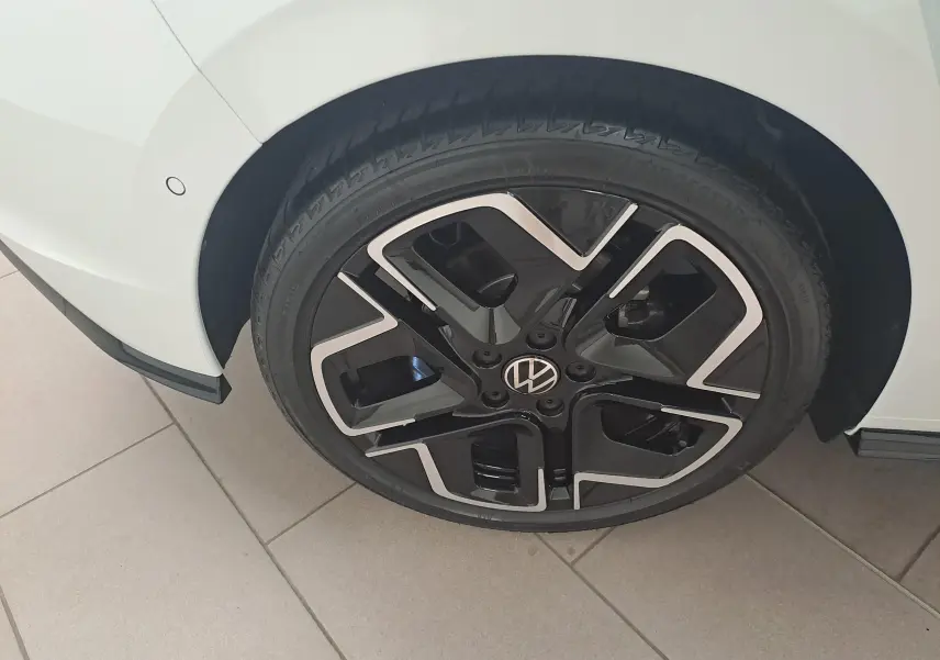 Gros plan sur la roue avant droite d'une Volkswagen Golf blanche avec jante noire et argentée au design moderne.