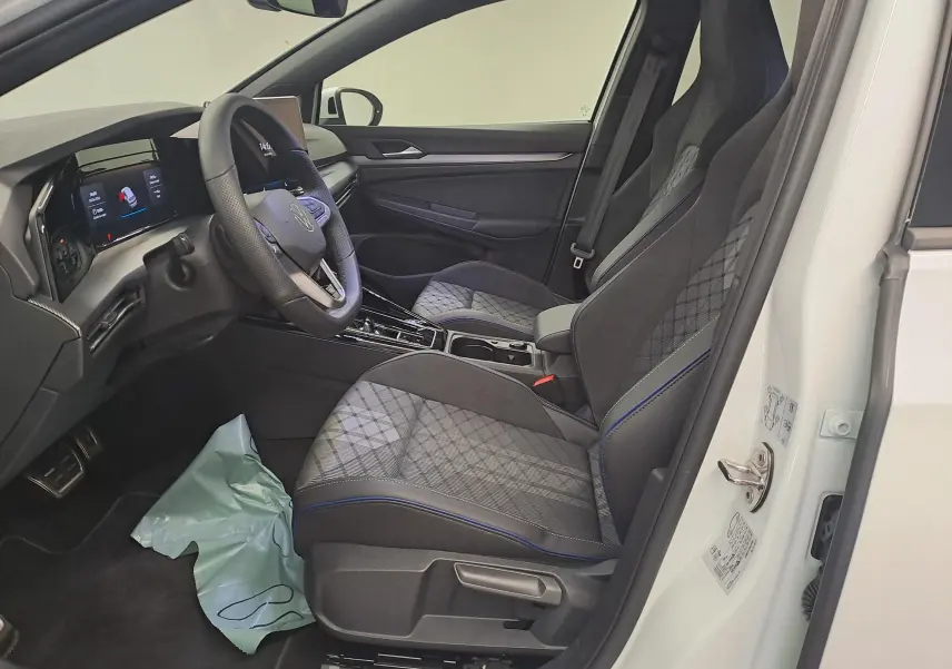 Vue intérieure côté conducteur de la Volkswagen Golf 2.0 TDI blanche, sièges tissu gris à surpiqûres bleues et volant cuir.