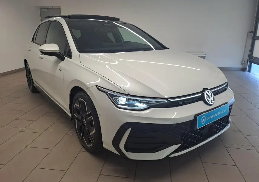 Vue 3/4 avant gauche d'une Volkswagen Golf blanche nacrée avec toit noir et phares LED allumés en intérieur.