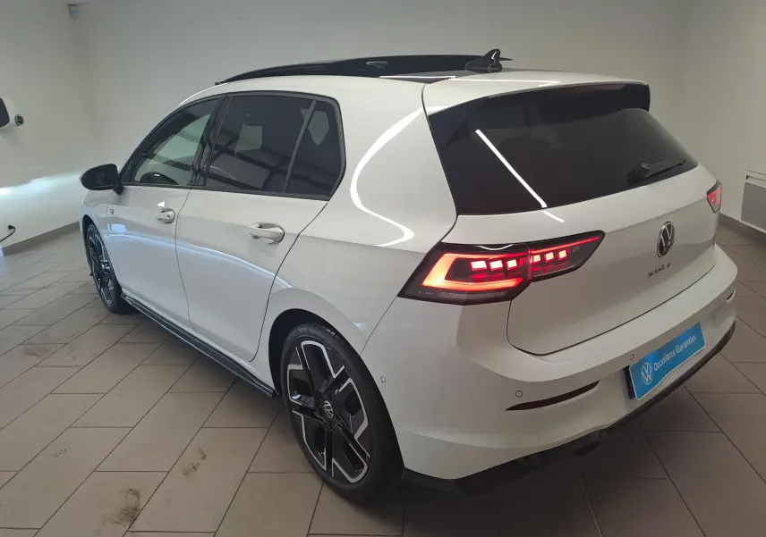 Vue 3/4 arrière gauche d'une Volkswagen Golf blanche nacrée avec toit noir, feux LED allumés et jantes noires stylées.