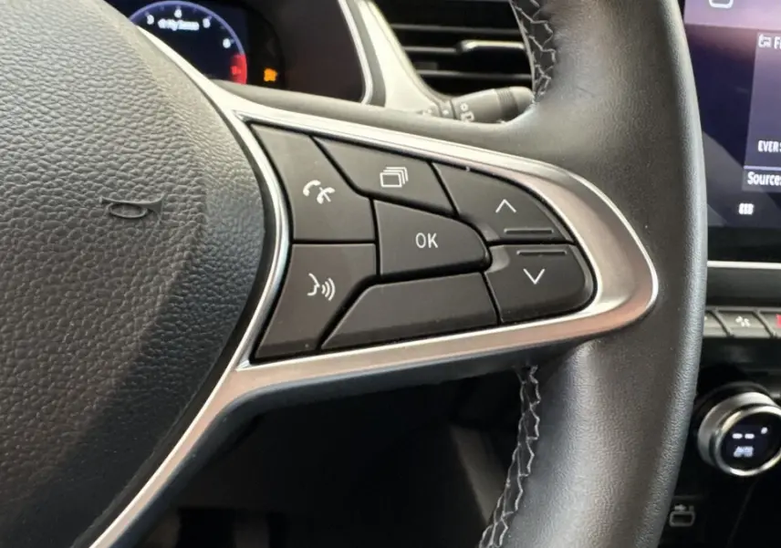 Gros plan sur les commandes au volant à droite du Renault Captur rouge 2024, avec écran tactile et tableau de bord partiel.