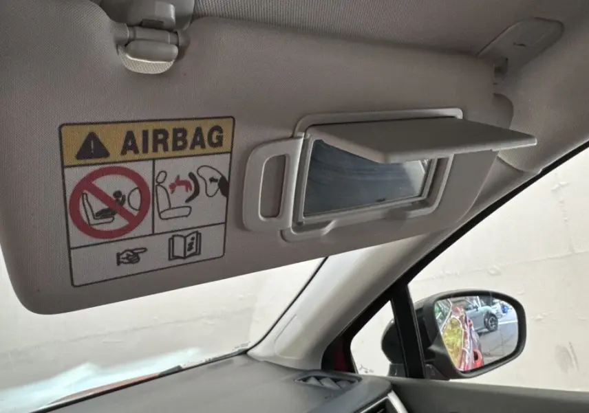 Vue intérieure côté conducteur du pare-soleil avec miroir et avertissement airbag, rétroviseur montrant la carrosserie rouge du Renault Captur.