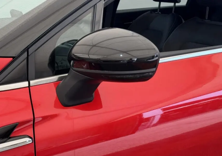 Gros plan sur le rétroviseur noir côté gauche d’un Renault Captur rouge 2024, avec fenêtre et partie de porte visibles.
