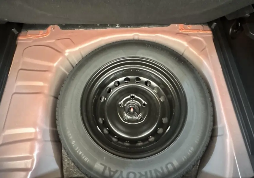Vue en plongée sur la roue de secours noire dans le compartiment arrière du Renault Captur rouge 2024.
