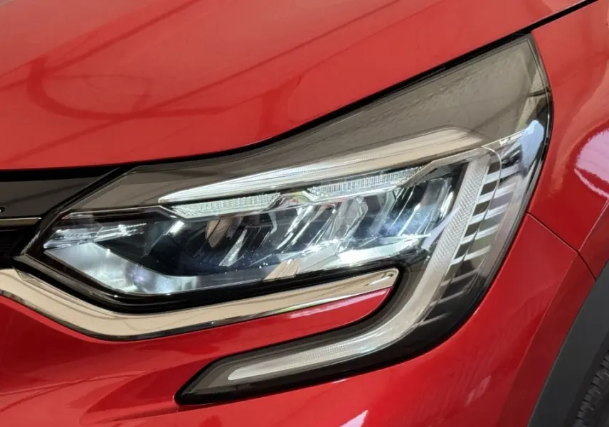 Gros plan sur le phare avant droit LED du Renault Captur rouge 2024 avec détails chromés et carrosserie brillante.
