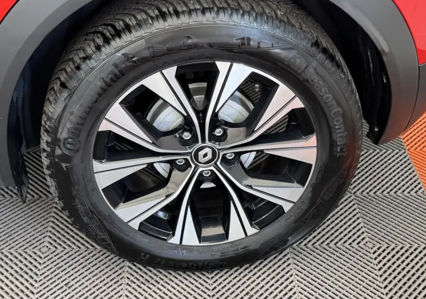 Gros plan sur la roue avant droite du Renault Captur rouge 2024 avec jante alliage bicolore et logo Renault central.