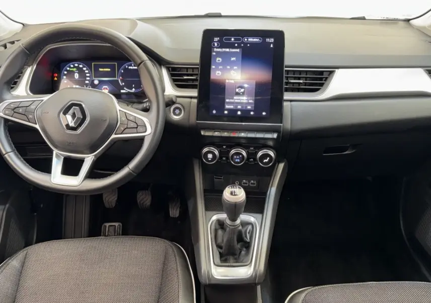 Vue intérieure avant du tableau de bord noir et gris du Renault Captur rouge 2024 avec écran tactile vertical et boîte manuelle.