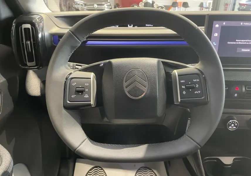 Vue rapprochée du volant noir gainé de la Citroën C3 2025 avec commandes intégrées et tableau de bord gris et bleu.